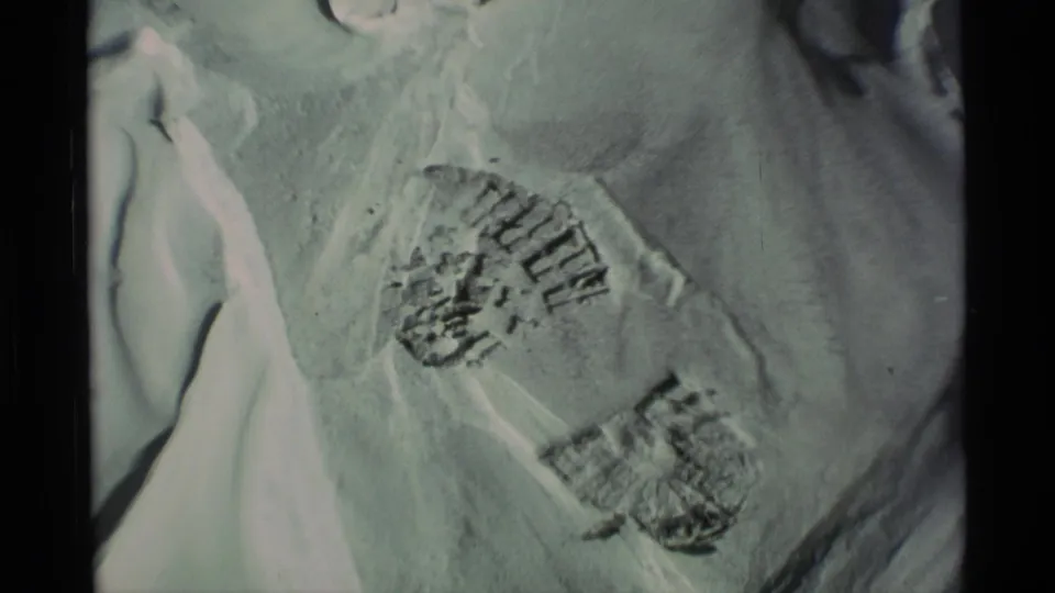 1977 Alaska 8mm frame showing close boot prints in snow with soft exposure and dark film borders.
