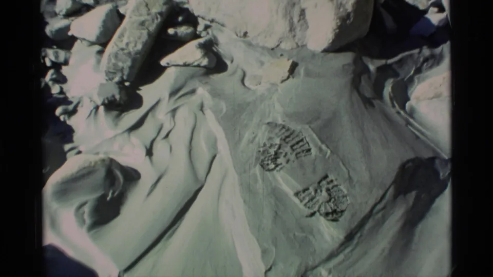 1977 Alaska 8mm frame of boot prints in snow with rocks at the edge of the close-up view.