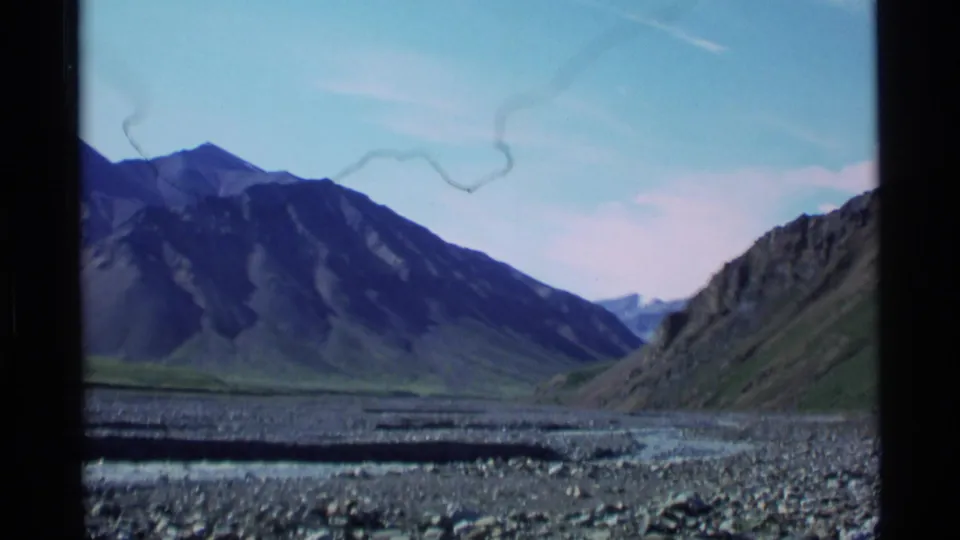 1977 Alaska 8mm view of a rocky riverbed and mountain valley beneath a clear blue sky.