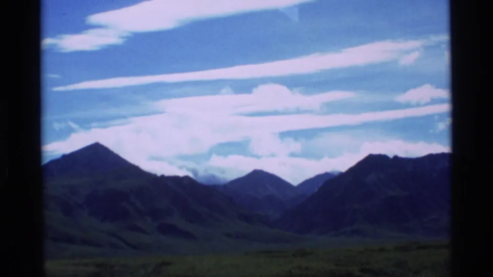 1977 Alaska 8mm landscape view of distant mountain ridges under a blue sky with long clouds.