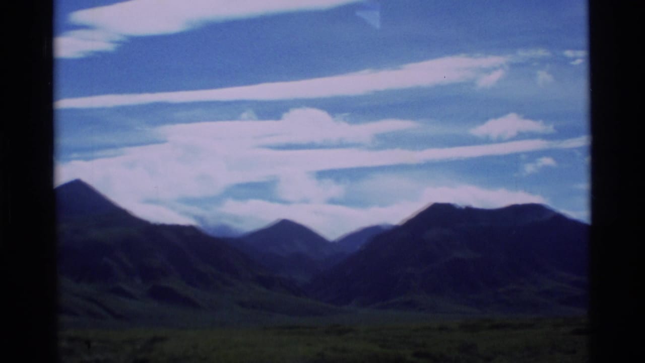 Mountain ridge beyond a grassy plain under blue sky and streaky clouds.