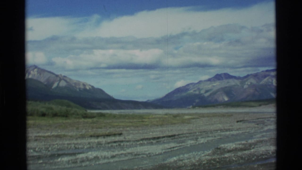 Wide gravel river valley with distant mountains under a cloudy blue sky.