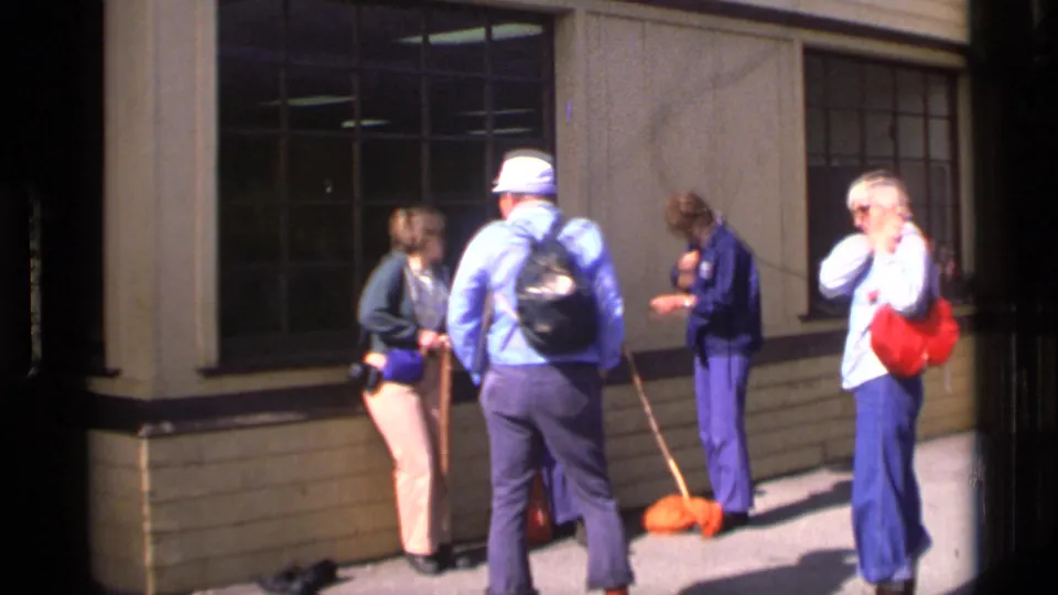 1977 Alaska travel footage shows four adults conversing near large windows outside a visitor building.