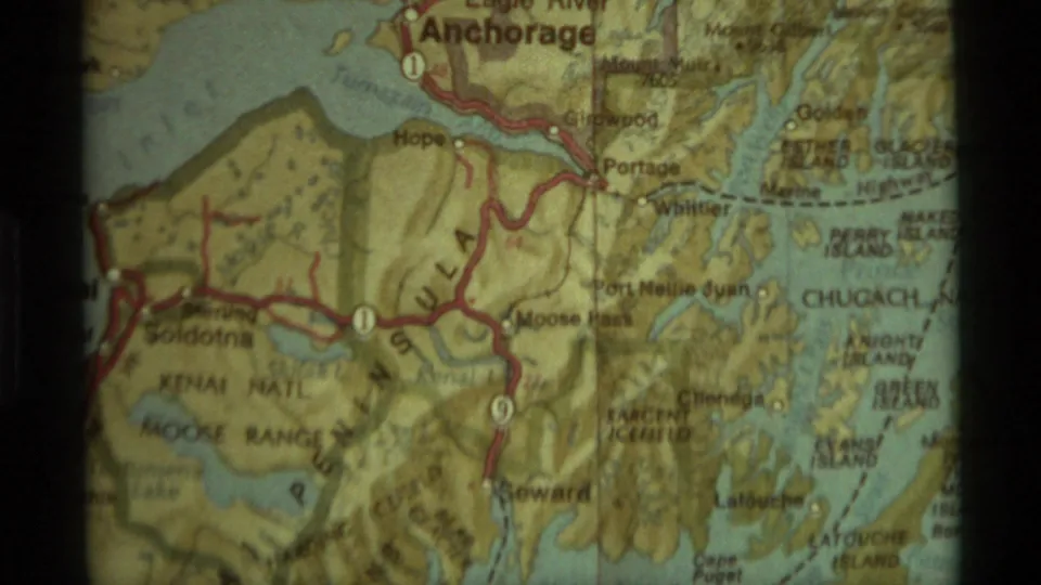 Close 8mm view of a printed Alaska map showing Anchorage and surrounding red road routes through mountain and coast areas.