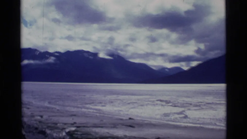 1977 Alaska 8mm frame of water in the foreground with a mountain range and layered clouds across the horizon.