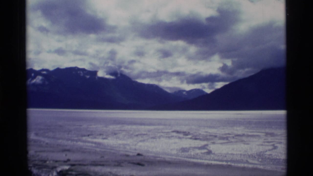 Flat icy landscape with distant mountains under heavy clouds.