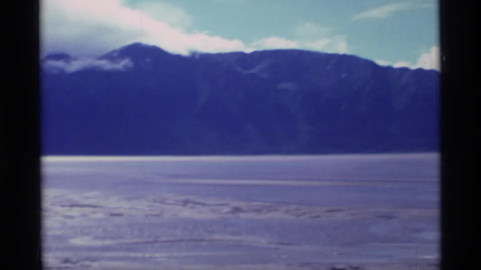 1977 Alaska 8mm view of a dark ridgeline above a pale frozen or tidal flat, with soft focus and visible film texture.