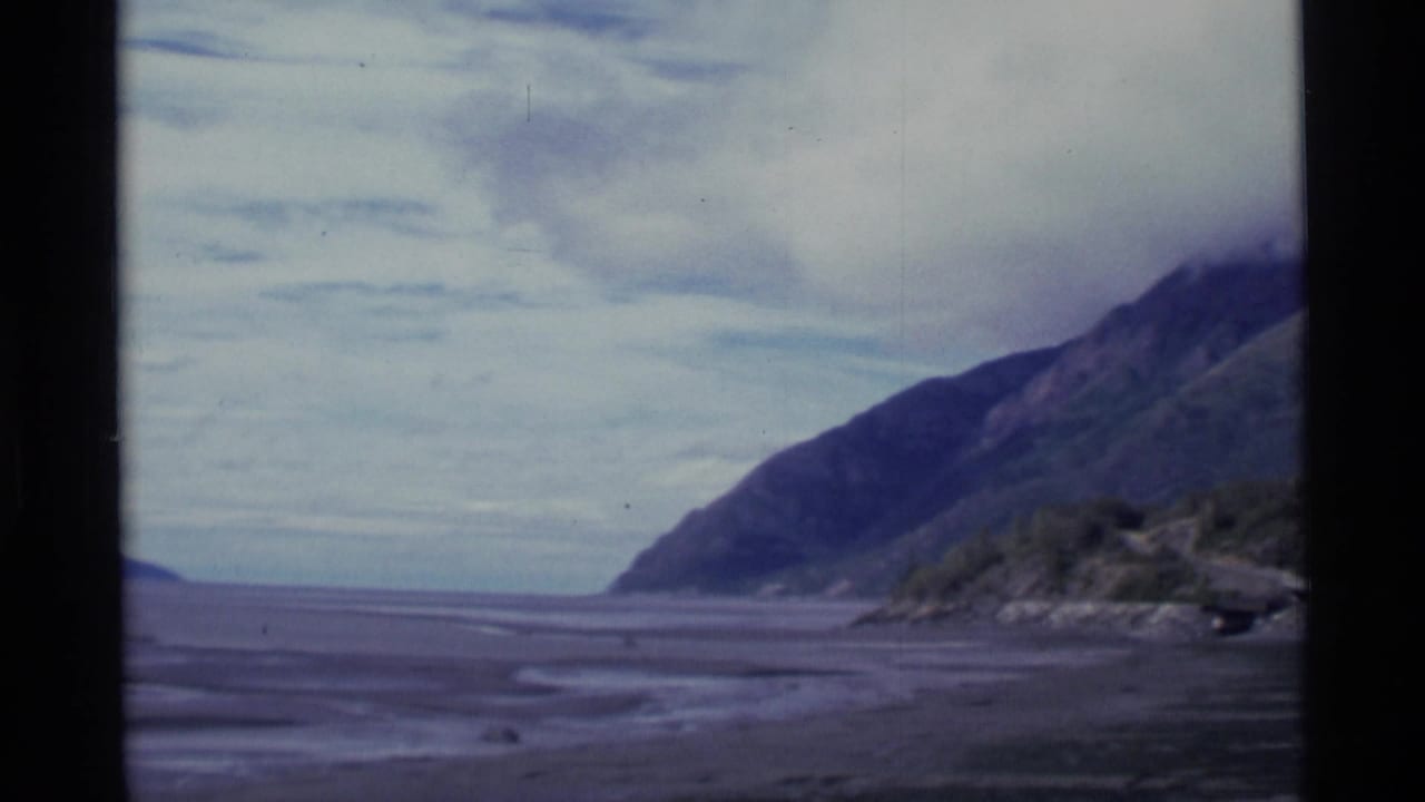 A wide flat shoreline or plain between mountain slopes under clouds.
