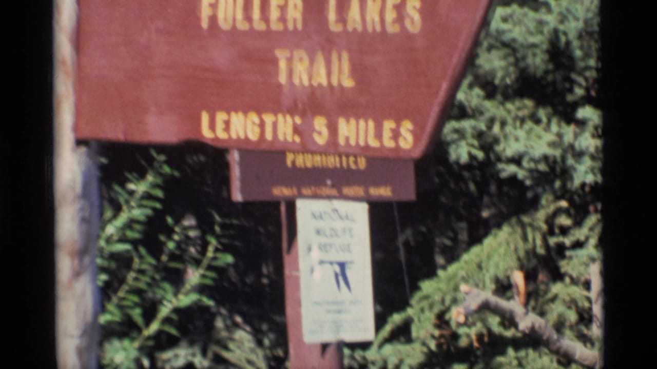 1977 Alaska frame showing Fuller Lakes Trail signage above a National Wildlife Refuge notice in dense greenery.