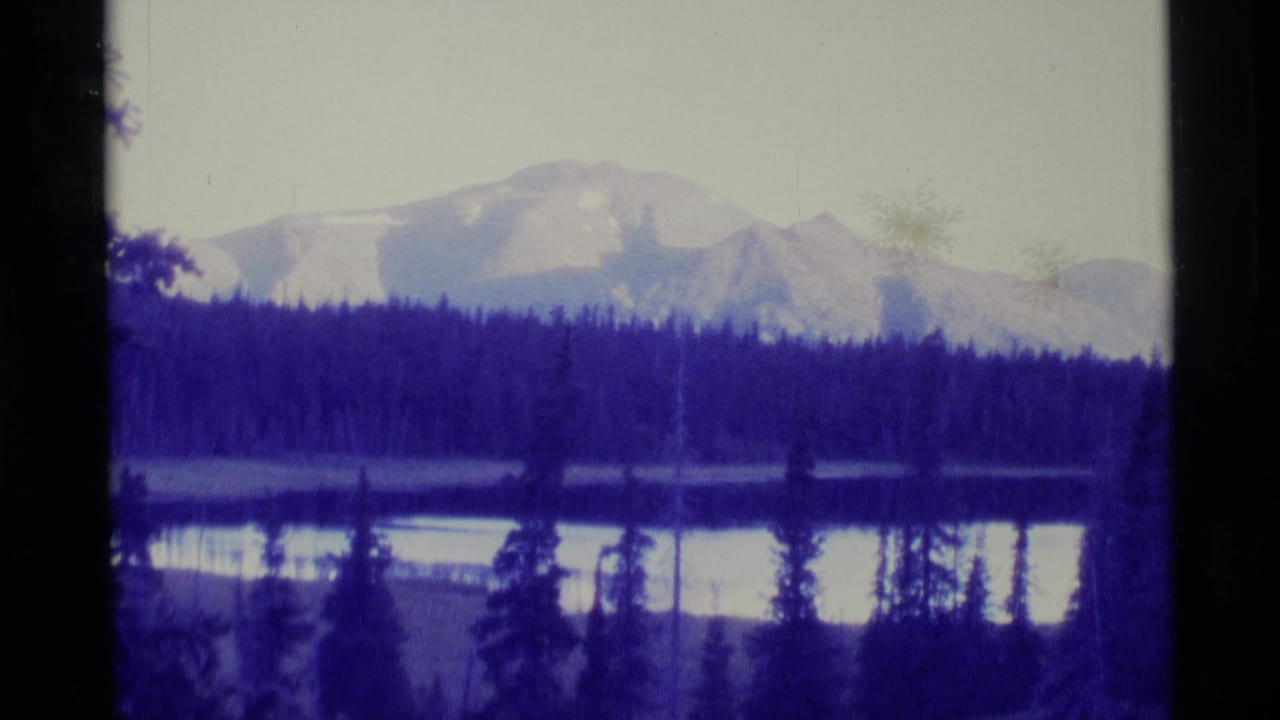 Lake bordered by dark evergreens with snow-capped mountains in the distance.