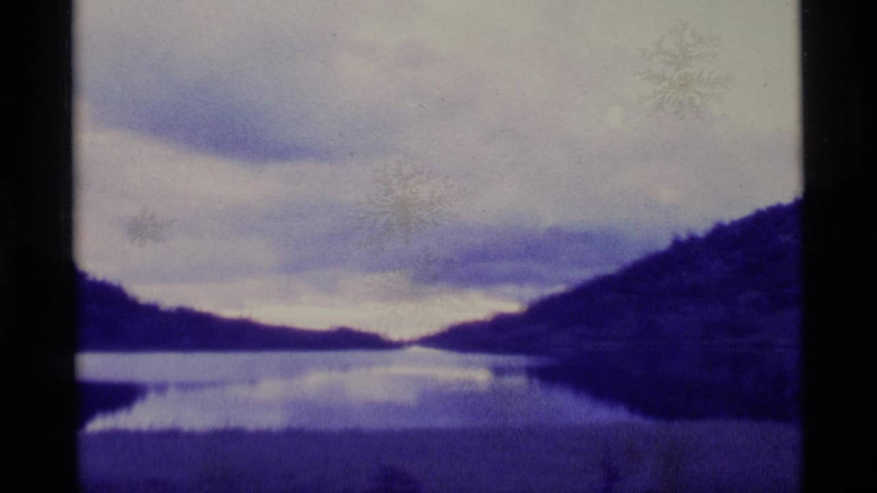 1977 Alaska home-movie view of a still lake bordered by forested hills beneath low cloud cover.