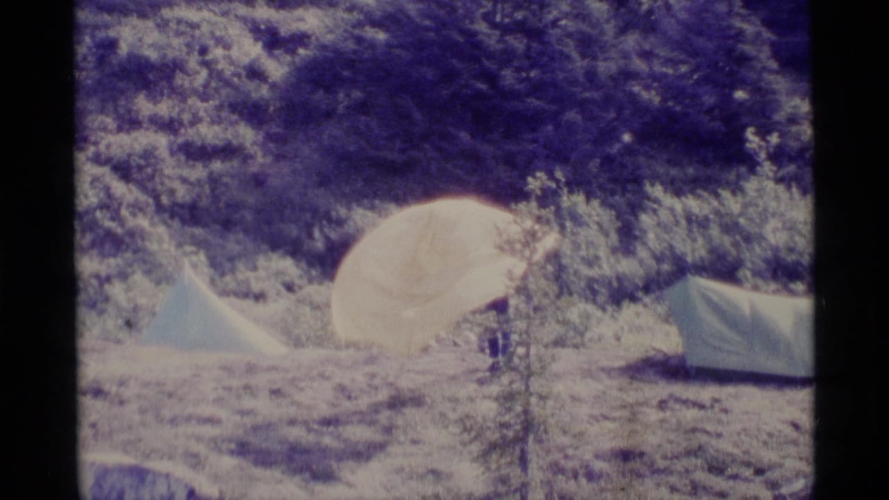 1977 Alaska 8mm frame showing pale tents in a campground clearing near dense evergreen trees.