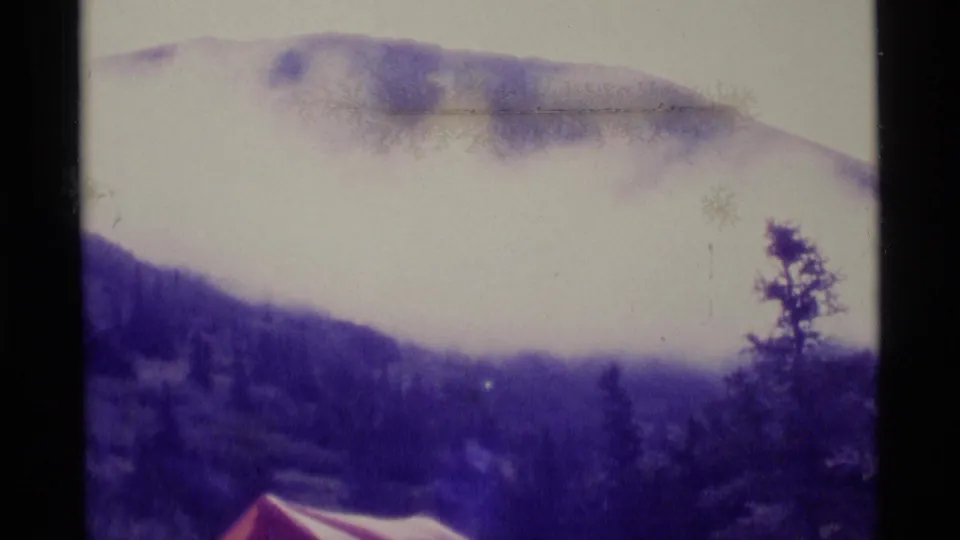 1977 Alaska 8mm frame where the camera frames a cloudy mountain above trees and the edge of a red tent.