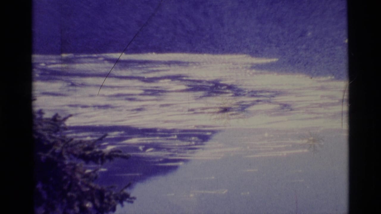 1977 Alaska 8mm frame showing snow or ice patterns below a deep blue sky, with silhouetted tree foliage near the lower left edge.