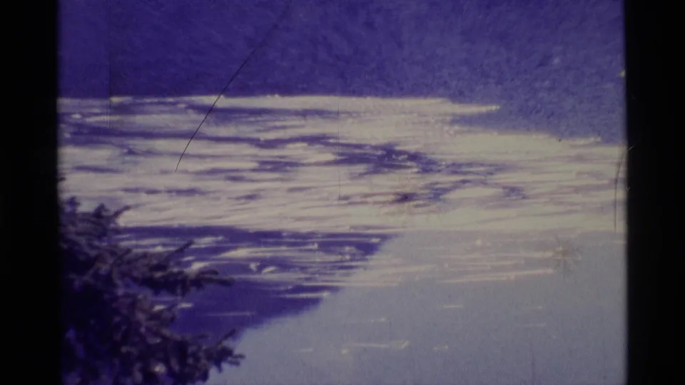 1977 Alaska 8mm frame showing snow or ice patterns below a deep blue sky, with silhouetted tree foliage near the lower left edge.