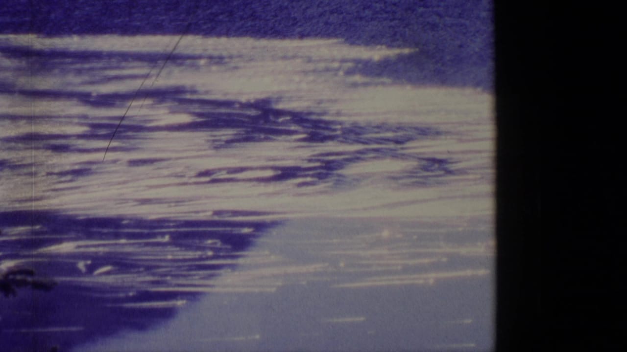 1977 Alaska 8mm frame with broad snow or ice streaks and darker bands across a frozen landscape below a blue sky.