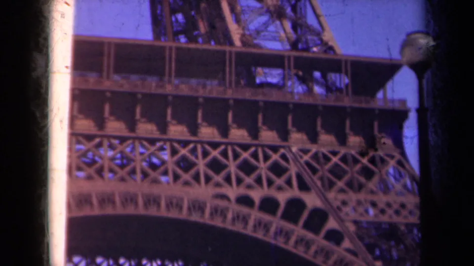 1939 Paris home-movie frame showing a close-up of Eiffel Tower latticework, platform railings, and blue sky.