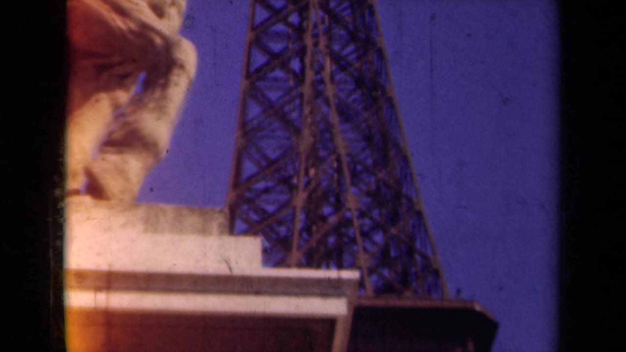 1939 Paris frame with the Eiffel Tower lattice and partial stone statue face in warm, grainy 8mm color.
