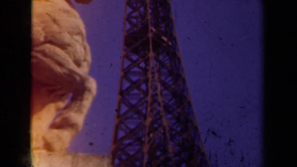 1939 Paris home-movie view looking up past a stone statue face toward the Eiffel Tower against the sky.