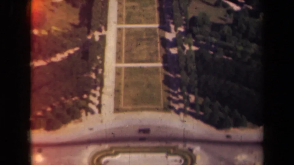 1939 Paris home-movie frame showing formal garden lawns, intersecting pale paths, and rows of dark trees from above.