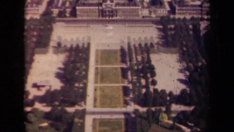 1939 Paris home-movie frame with formal lawns, tree allees, paths, and a large building beyond the garden.