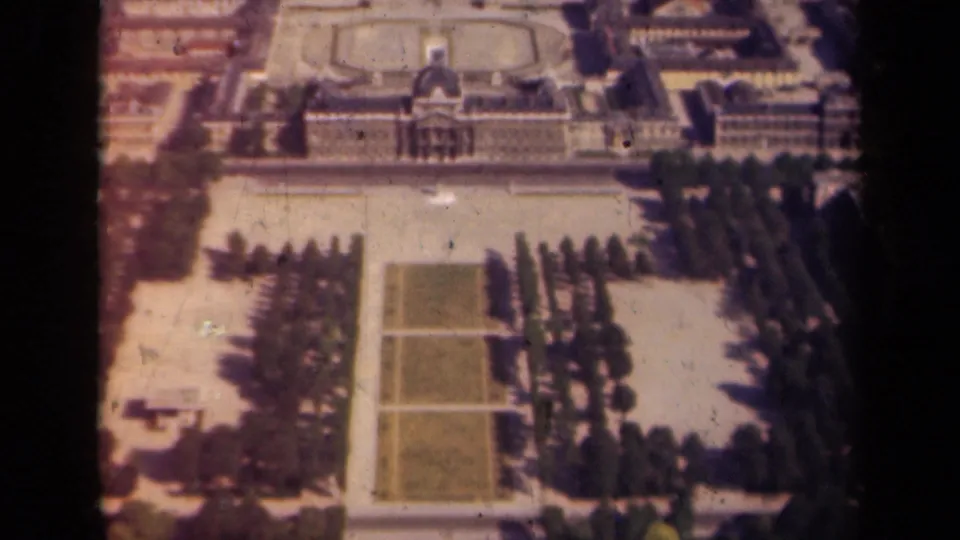 1939 Paris aerial home-movie frame looking down over a monumental building, rectangular lawns, tree rows, and surrounding grounds.