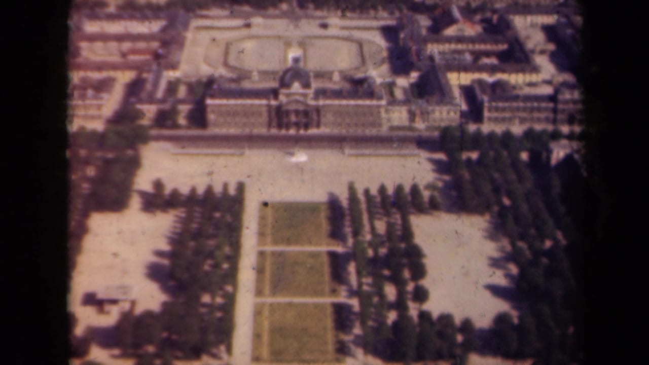 1939 Paris frame showing the same elevated view across clipped lawns, aligned trees, paved garden walks, and a palace-like facade.