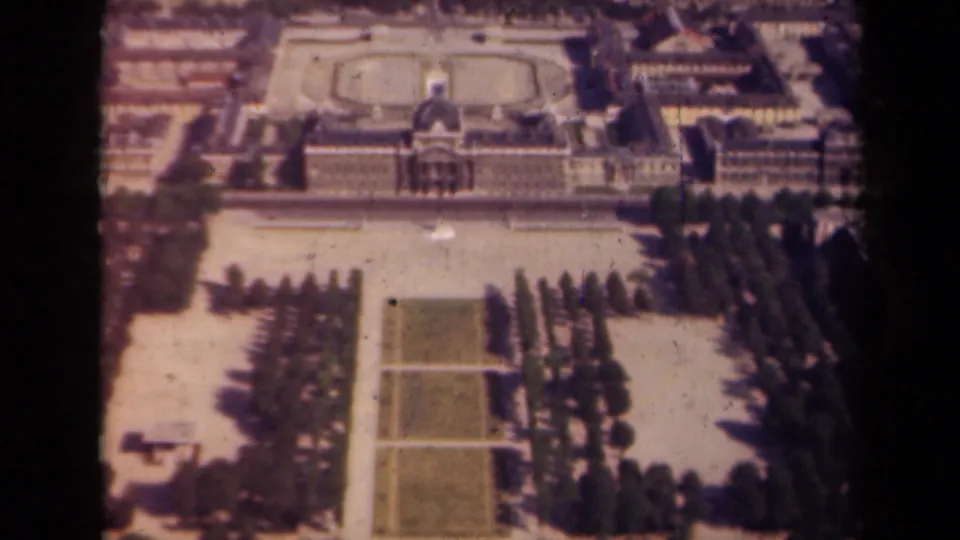 1939 Paris frame showing the same elevated view across clipped lawns, aligned trees, paved garden walks, and a palace-like facade.