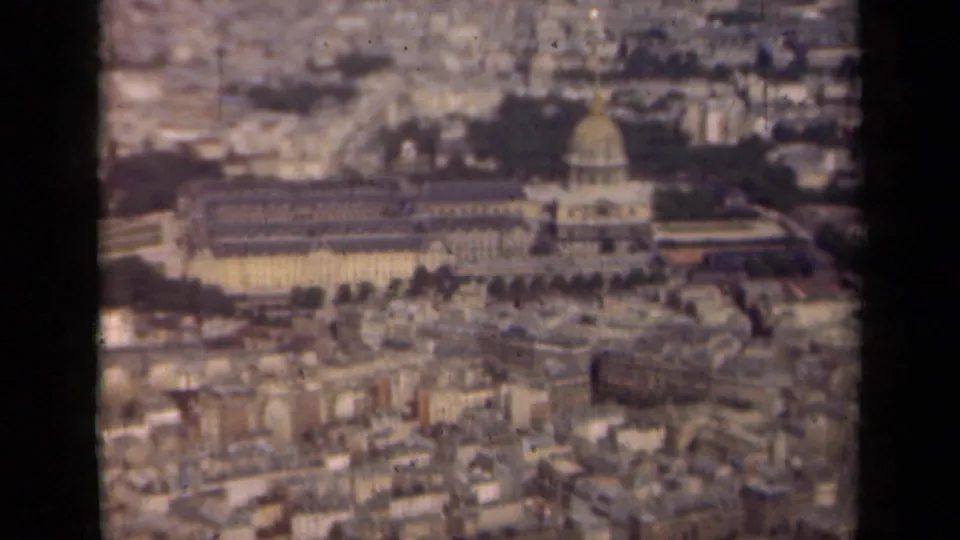 1939 Paris aerial frame with a domed structure, surrounding urban rooftops, trees, and softened 8mm color and grain.