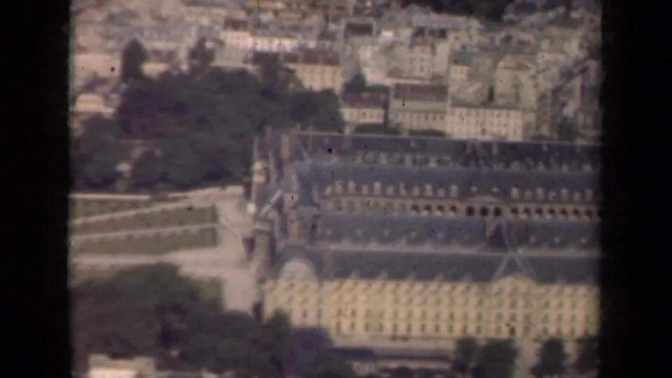 1939 Paris frame showing the Invalides grounds from above, with long building wings, paths, trees, and dense city rooftops beyond.