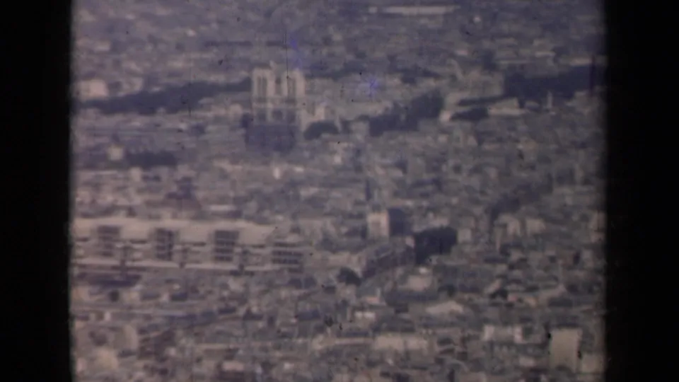 1939 Paris aerial view showing Notre-Dame Cathedral rising above dense rooftops, with soft focus and visible film wear.