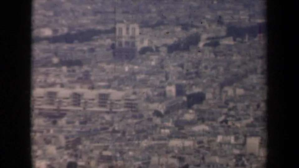 Paris aerial frame from 1939 showing Notre-Dame Cathedral amid dense city blocks, viewed through a dark aircraft-window edge.