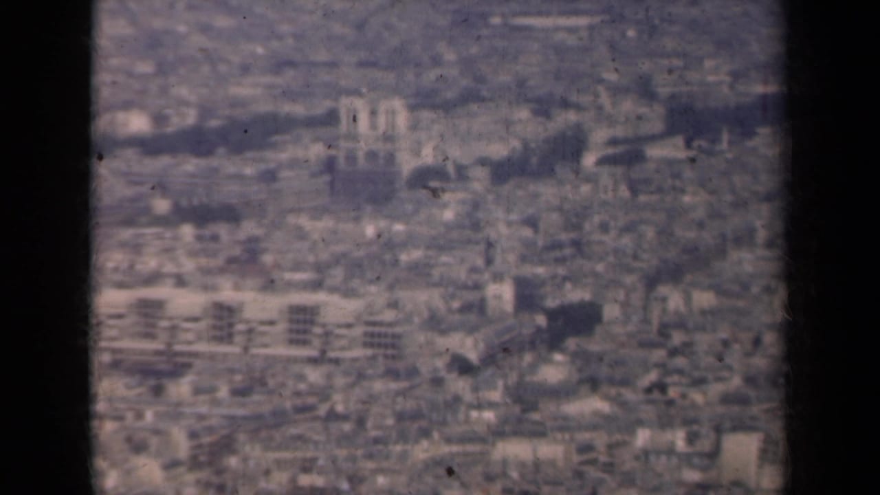 1939 Paris cityscape from above, with twin cathedral-like towers, dense buildings, and muted color from 8mm film.