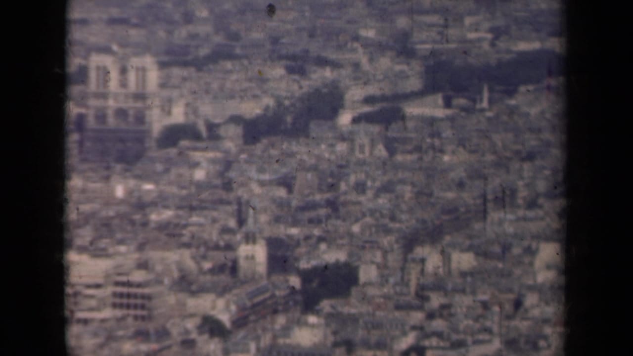 Blurred aerial view over central Paris rooftops with Notre-Dame in the distance.