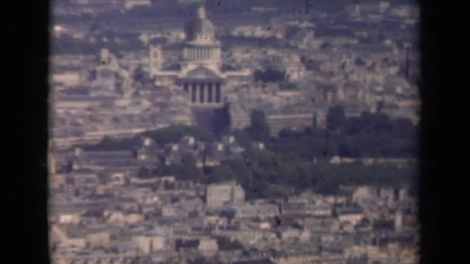 1939 Paris high-vantage frame with a domed landmark, colonnaded building front, surrounding rooftops, and dark green grounds.