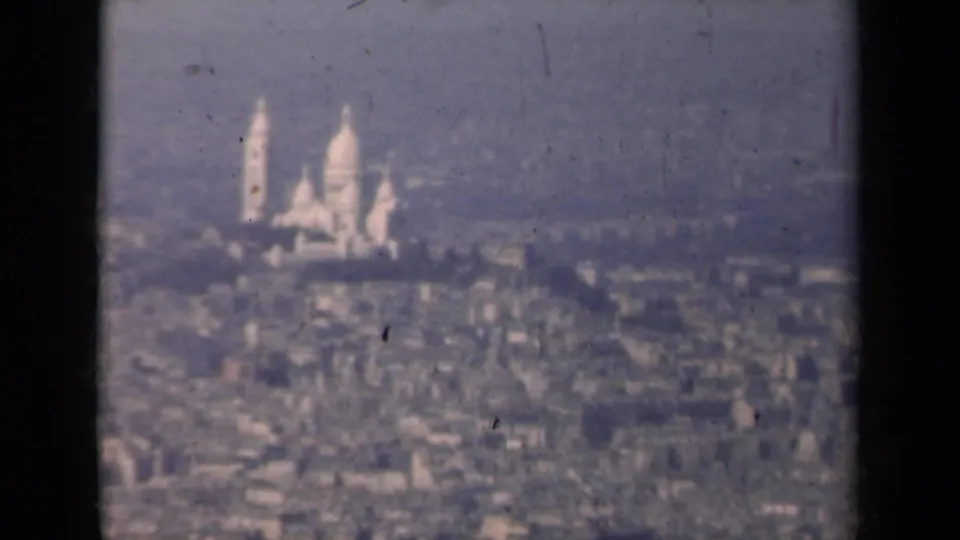 1939 Paris home-movie frame showing Sacre-Coeur on Montmartre through haze, with rooftops in the foreground.