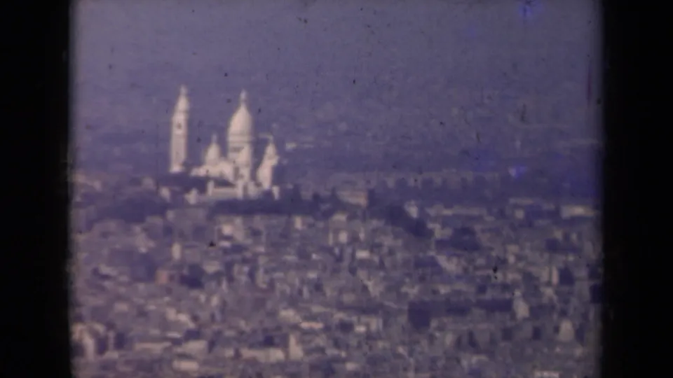 Late-1930s Paris frame with Sacre-Coeur visible on Montmartre, softened by haze and small-gauge film texture.