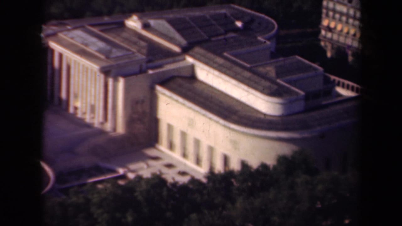 1939 Paris view from above showing the columned side of a modernist building, curved roof forms, trees, and background city blocks.