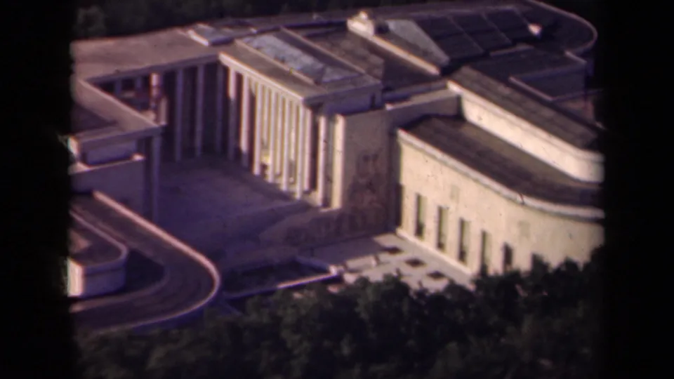 1939 Paris high-angle frame with tall columns, a broad paved forecourt or terrace, curved edge lines, trees, and layered roofs.