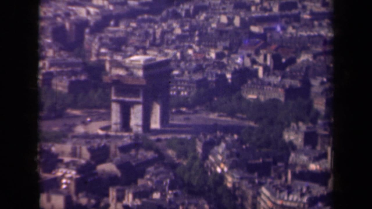 1939 Paris 8mm frame showing the Arc de Triomphe from above, with nearby avenues, rooftops, and trees softened by film grain.