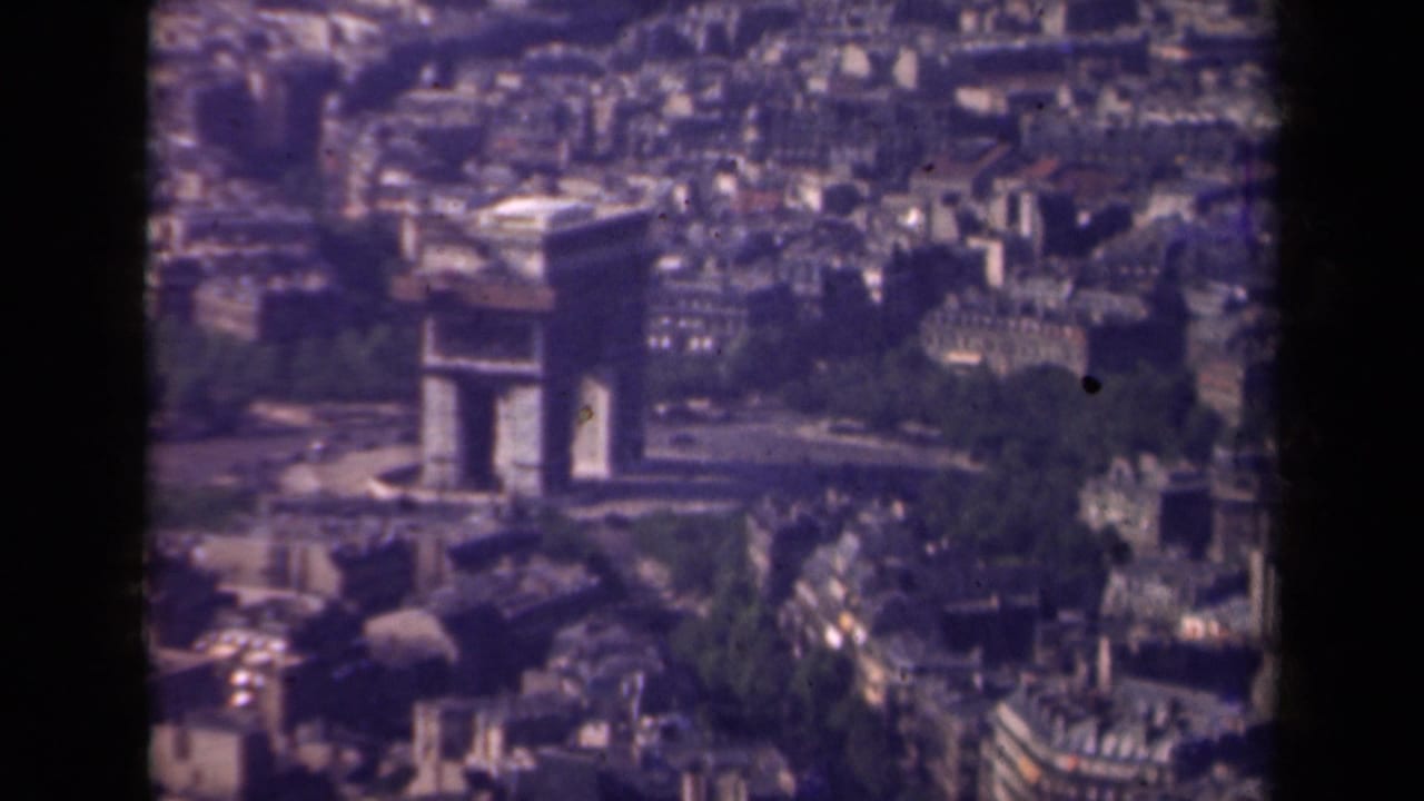 High-angle 1939 Paris view with the Arc de Triomphe near center, surrounded by city blocks, avenues, and softened 8mm color.