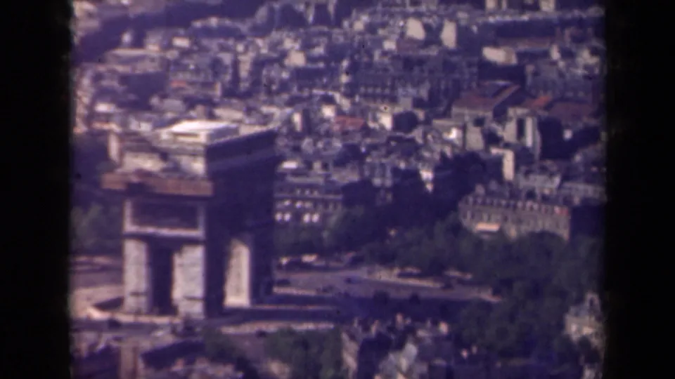 1939 elevated Paris view showing the Arc de Triomphe, a traffic circle, trees, and dense city buildings on faded 8mm film.