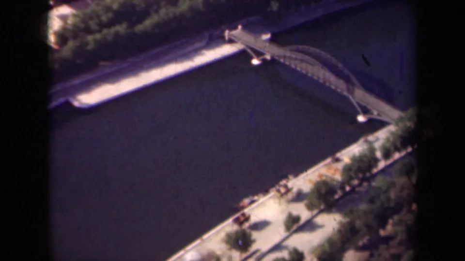 1939 Paris home-movie frame showing an elevated view of an arched bridge over a broad river, bordered by trees and embankment paths.
