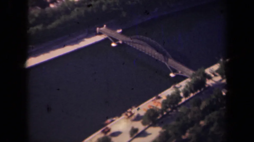Paris aerial home-movie frame with the bridge crossing the river diagonally, trees along the embankment, and visible 8mm scan borders.
