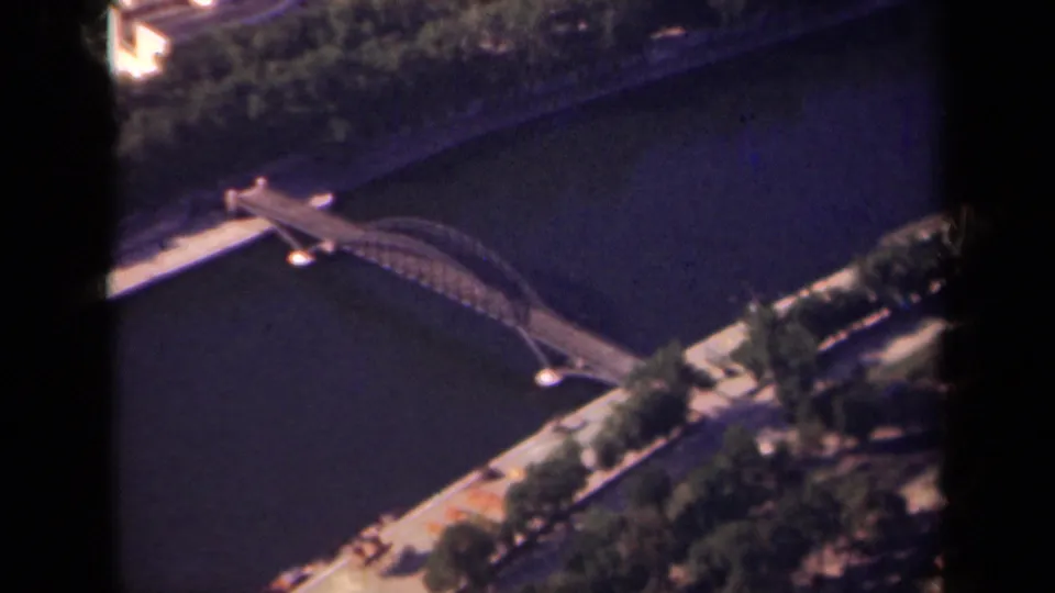 Elevated 1939 Paris frame showing a curved arched bridge over the river, tree-lined embankments, and the dark edge of the film frame.