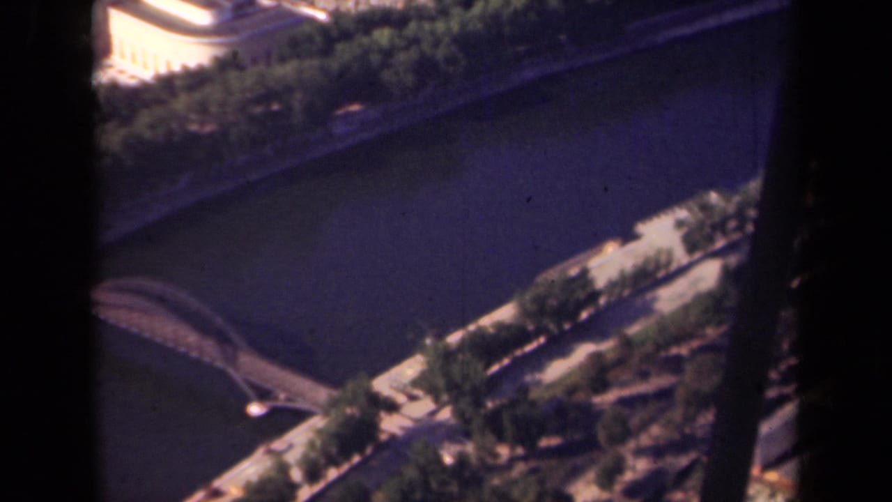 1939 Paris footage looking down on the Seine with a bridge, embankment trees, riverside roadway, and city buildings.