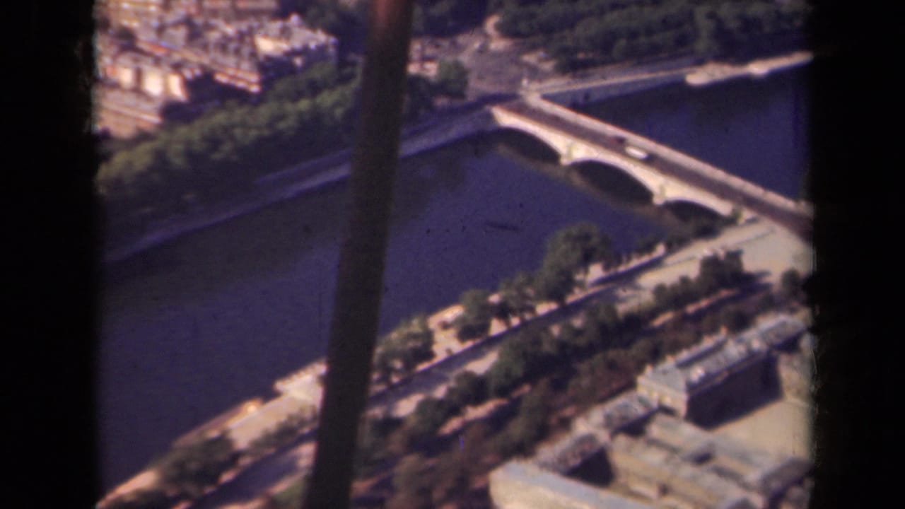 1939 Paris high-angle view showing the Seine, an arched bridge, embankment roads, trees, and pale city buildings through dark frame edges.
