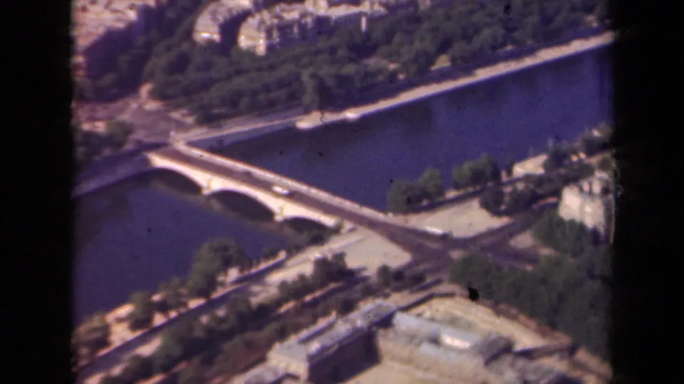 1939 Paris oblique aerial frame showing the Seine, an arched bridge, road junctions, trees, and urban blocks with soft 8mm texture.