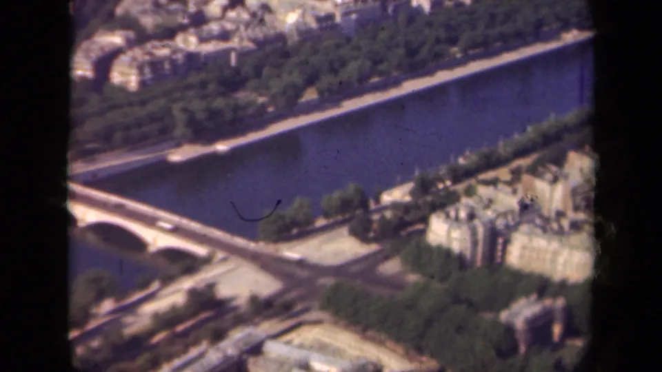 1939 Paris high-angle view of the Seine and bridge area, with riverbank roads, tree rows, pale buildings, and visible dust marks on the film.