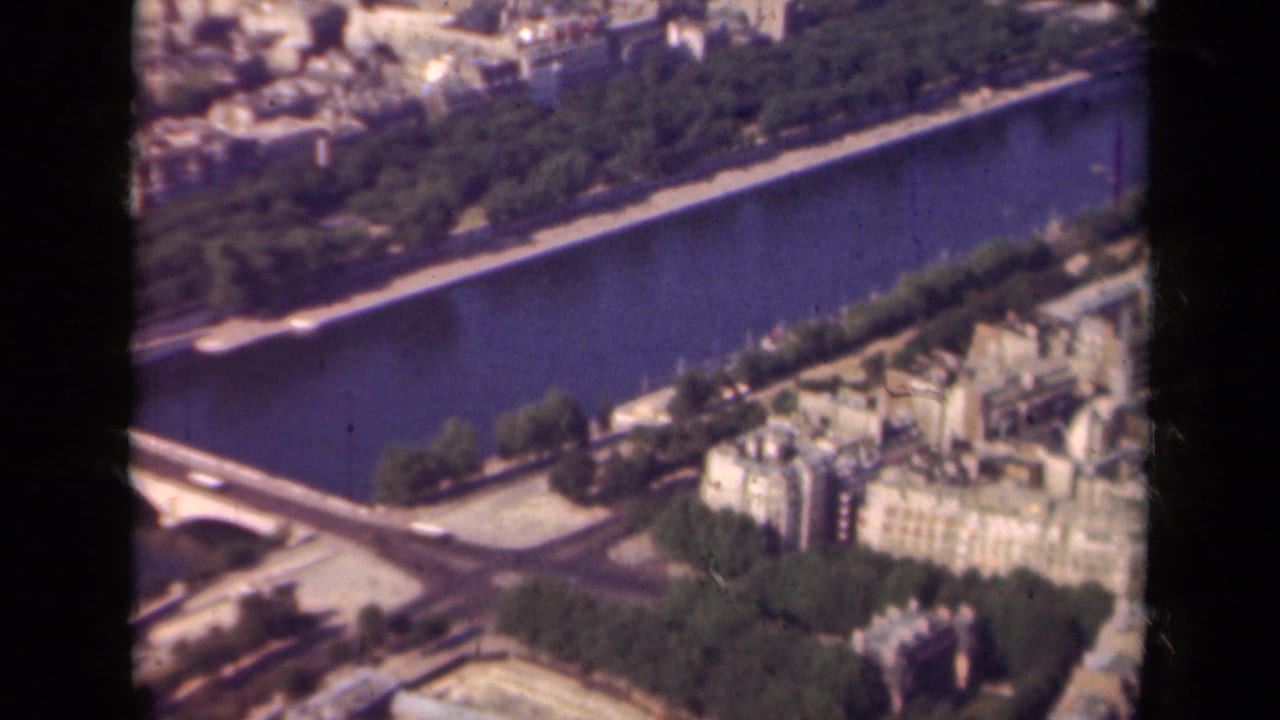 1939 Paris aerial frame showing the Seine, a bridge crossing, tree-lined quays, and pale urban blocks seen through 8mm film edges.